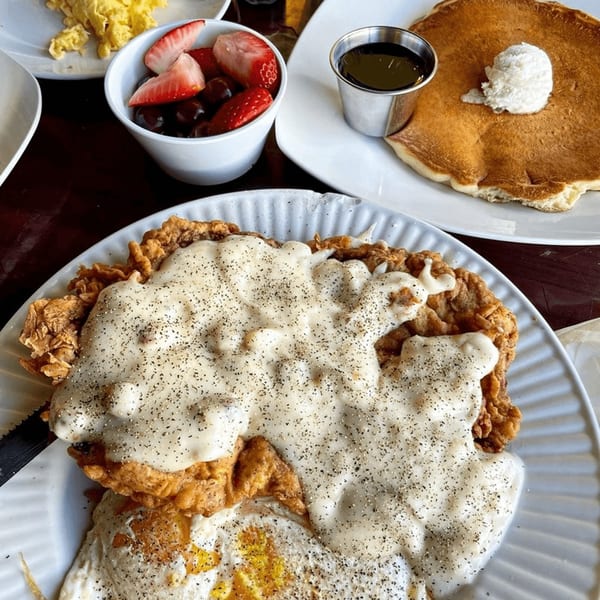 Chicken fried steak with gravy and eggs, alongside pancakes, fruit, and scrambled eggs.