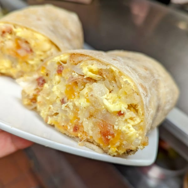 A breakfast burrito from Aunt Yese's Home Cooking, cut in half, revealing eggs, cheese, and bacon.
