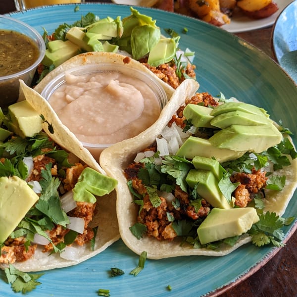 Three tacos with meat, cilantro, onions, and avocado slices, with sides of salsa and refried beans.