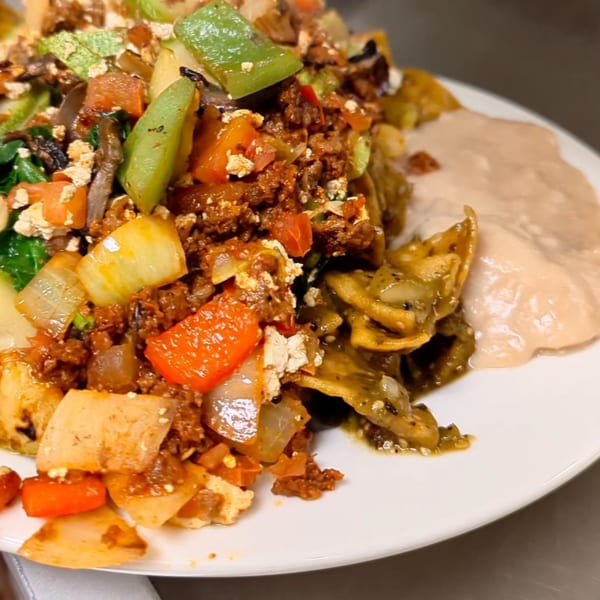 A close-up of a plate of chilaquiles with red and green peppers, onions, and refried beans.