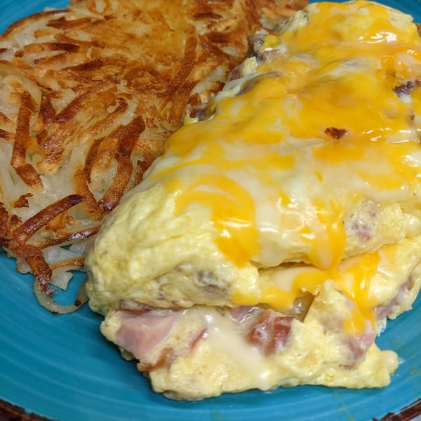 A cheesy omelet with ham and hash browns on a blue plate at Aunt Yese's Home Cooking.