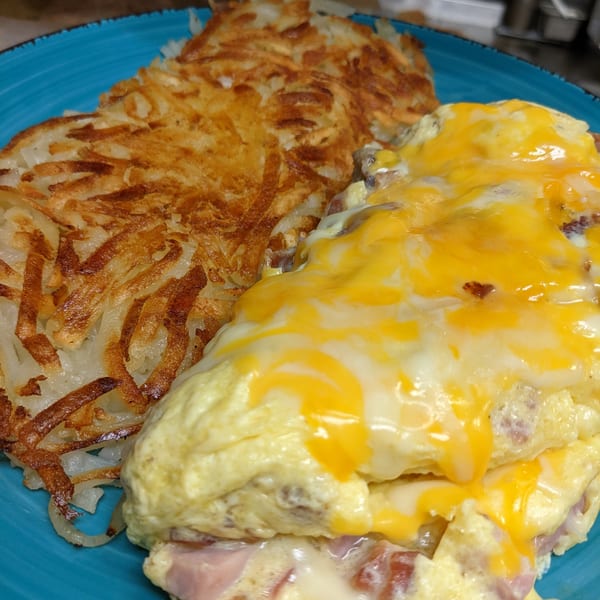 Aunt Yese's Home Cooking breakfast with a cheesy omelet and crispy hash browns on a blue plate.