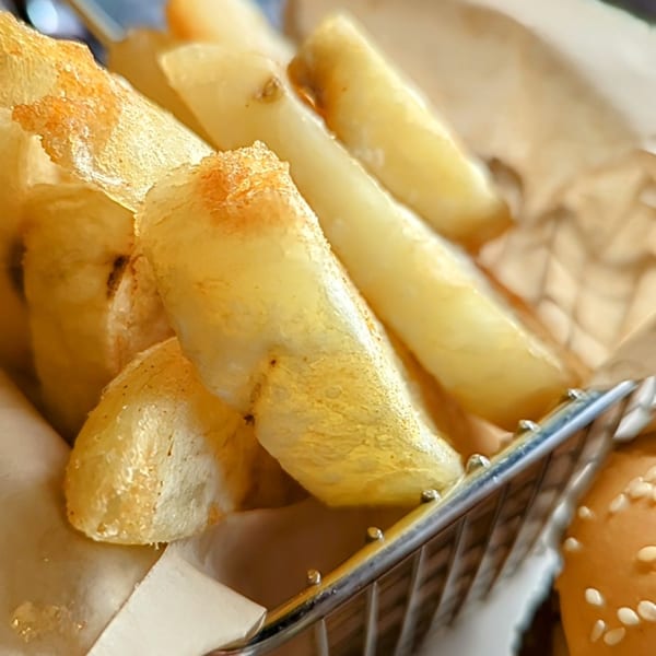 Close-up of golden, crispy steak fries in a metal basket, with a burger bun visible.