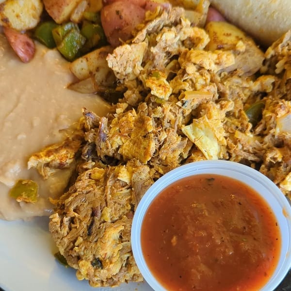 A breakfast plate with scrambled eggs, potatoes, refried beans, and a side of salsa.