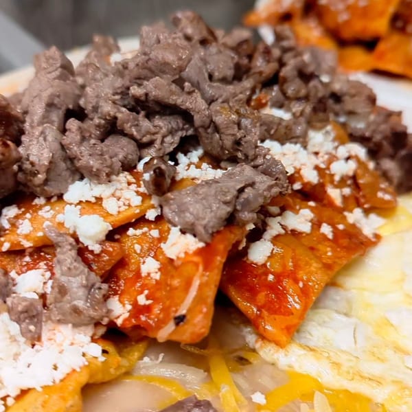 Close-up of chilaquiles with red sauce, crumbled cheese, and shredded beef.