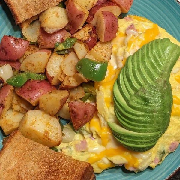Aunt Yese's breakfast plate with a cheesy omelet topped with avocado, home fries, and toast.