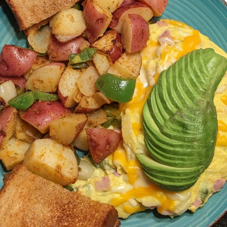 Aunt Yese's breakfast plate with a cheesy omelet topped with avocado, home fries, and toast.