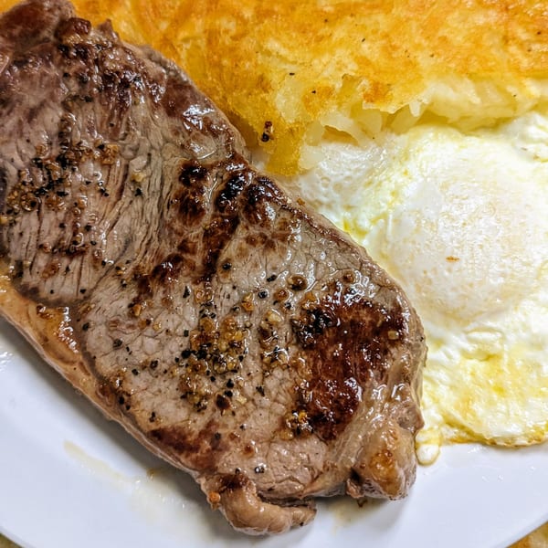 Aunt Yese's Home Cooking steak and eggs with hash browns on a white plate.