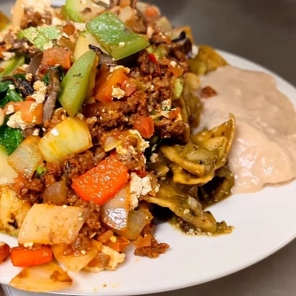 A close-up of a colorful American dish with meat, vegetables, and a side of creamy sauce.