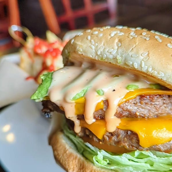 Close-up of a double cheeseburger with special sauce, lettuce, and sesame seed bun, with fries in background.