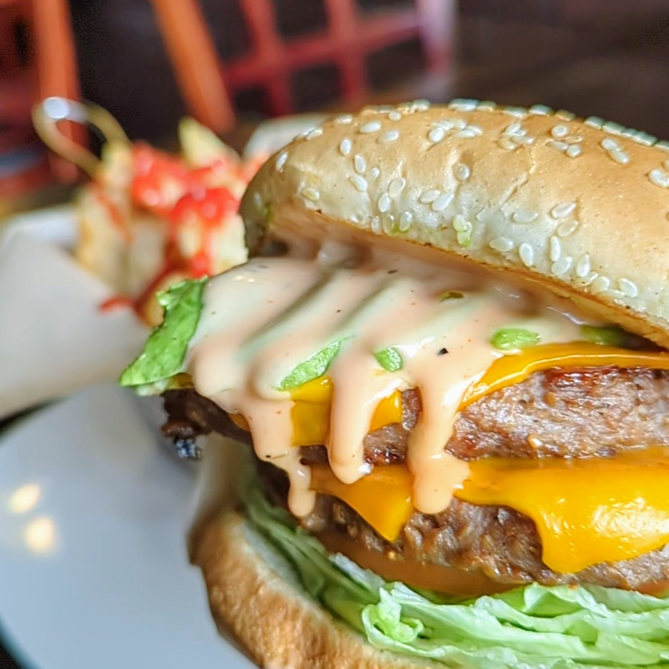 Close-up of a double cheeseburger with special sauce, lettuce, and sesame seed bun, with fries in background.